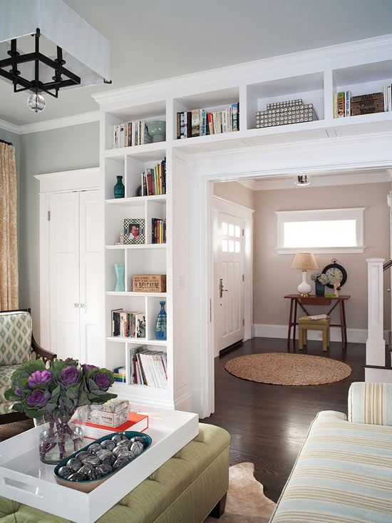 a living room filled with furniture and bookshelves next to a doorway that leads to another room