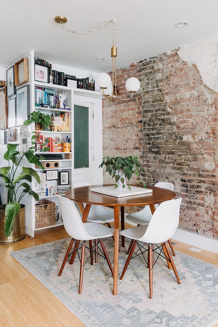 a dining room with brick walls and wooden table surrounded by white chairs, potted plants and bookshelves