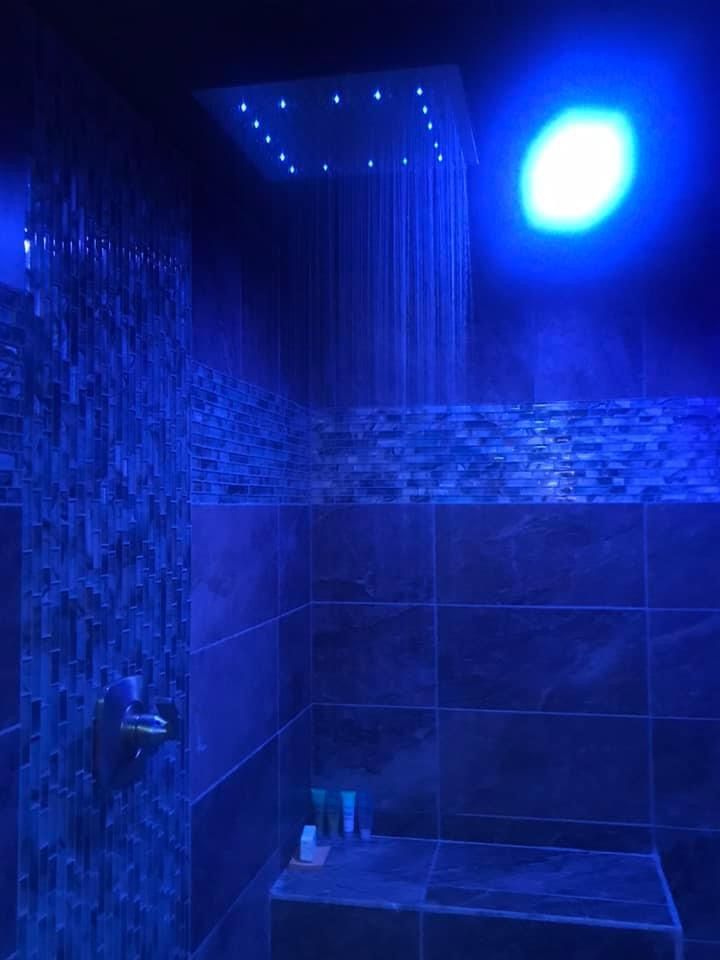 a shower head with blue lights on the ceiling and tiled walls in a dark bathroom