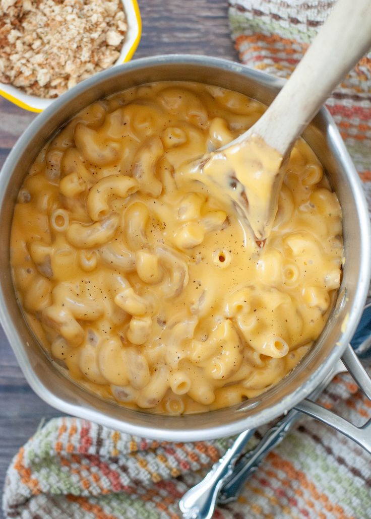 a ladle full of macaroni and cheese being stirred with a wooden spoon