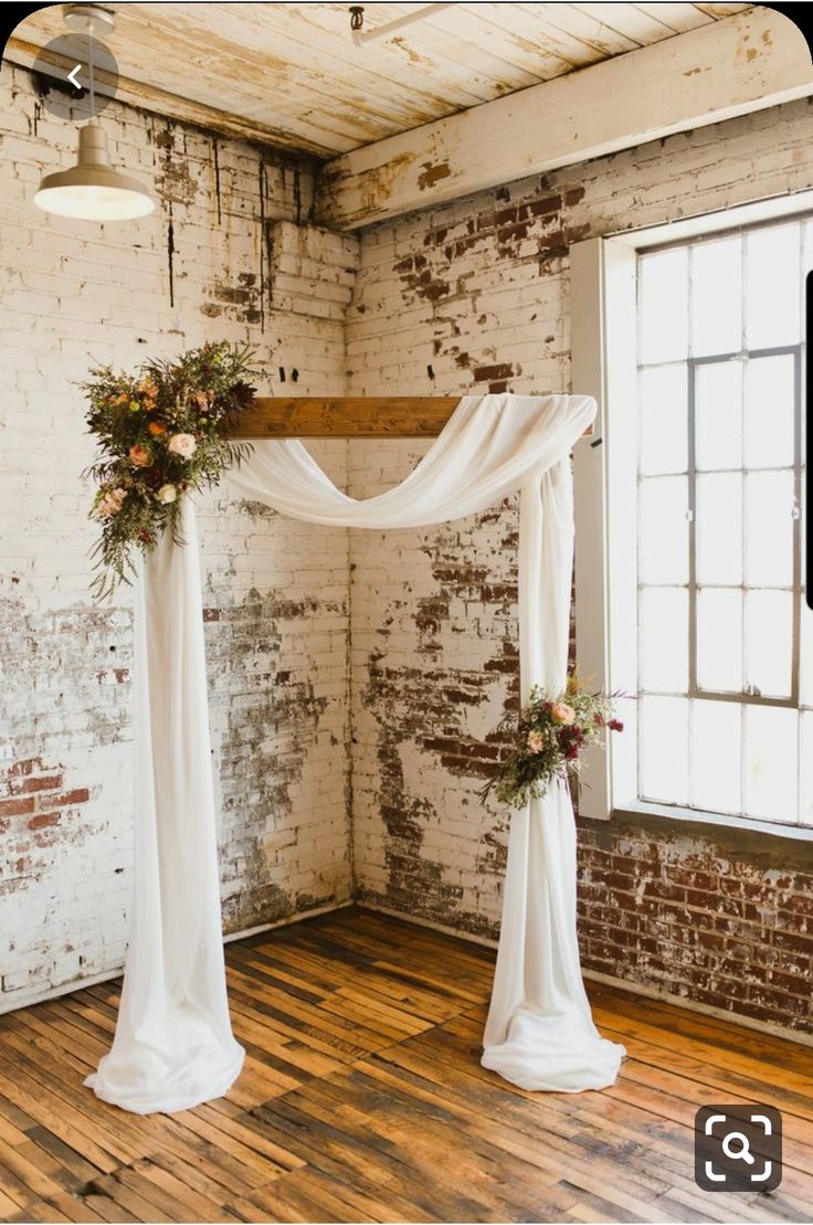 the wedding arch is decorated with greenery and white draping, along with flowers