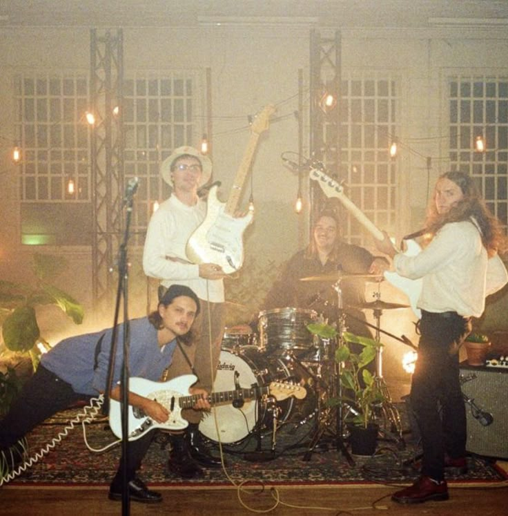 three people are playing guitars and singing in front of microphones while another person is standing behind them