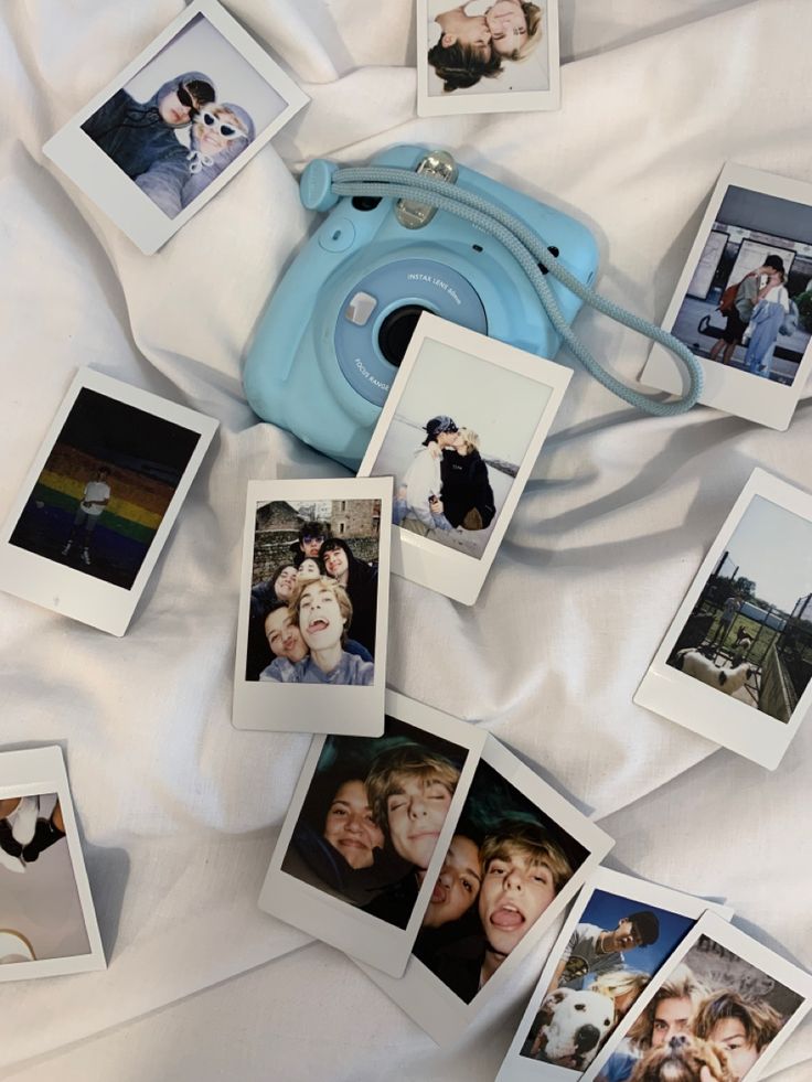 several polaroid photos are arranged on a bed with white sheets and a blue camera