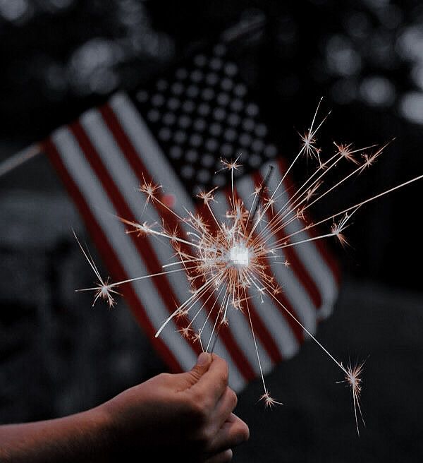 someone holding a sparkler in front of an american flag