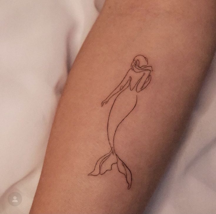 a woman's arm with a tattoo of a mermaid holding a ballon d'or