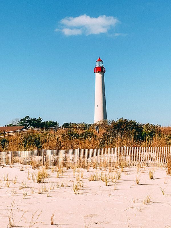 a light house sitting on top of a sandy beach next to a wooden picket fence