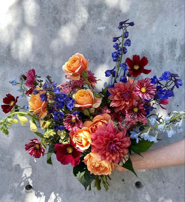 a bouquet of flowers in someone's hand on a concrete surface with sunlight coming through the leaves