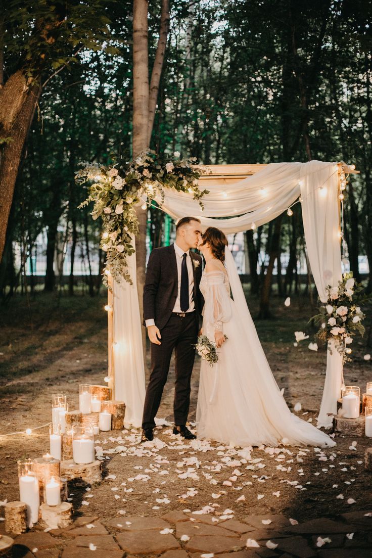 a bride and groom kissing in front of their wedding arch with candles on the ground