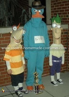 three children in costumes standing next to each other on the sidewalk with one person wearing an orange and blue costume