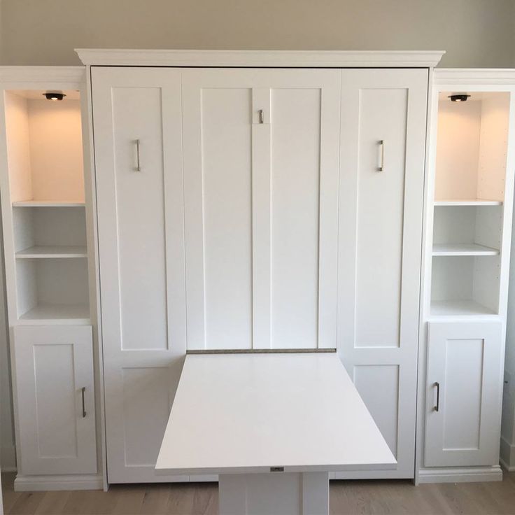 an empty room with white cupboards and a table in front of the bookshelves