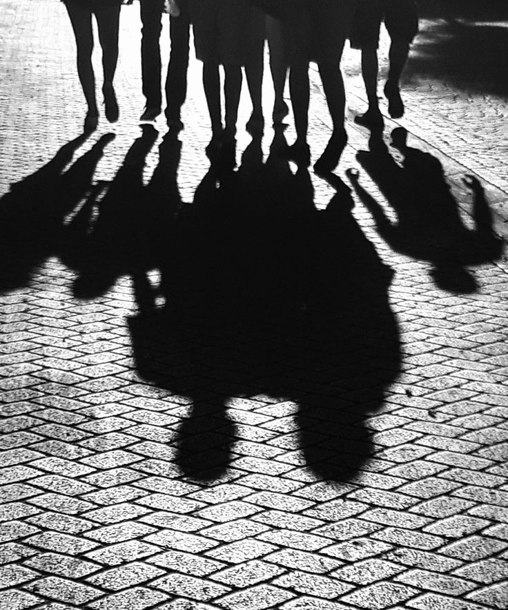 a group of people walking down a street with their shadows on the ground behind them