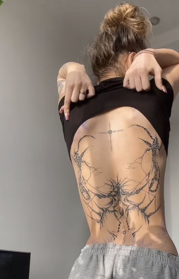 the back of a woman with tattoos on her body and behind her is a laptop