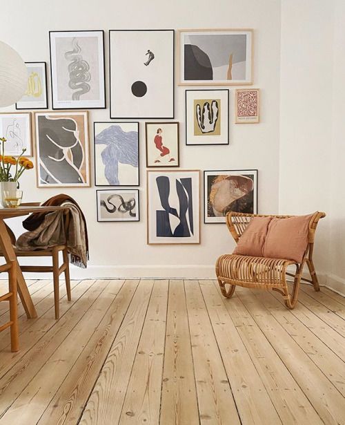 a living room filled with lots of pictures on the wall and wooden chairs in front of it