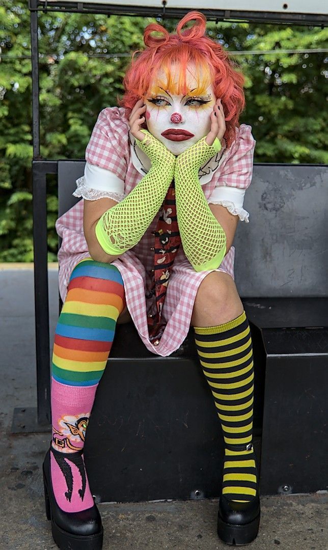 a woman with red hair and makeup is sitting on a bench wearing colorful tights