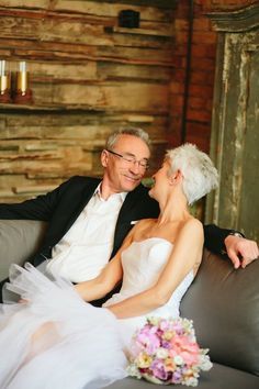 a bride and groom sitting on a couch in front of a wooden wall with candles