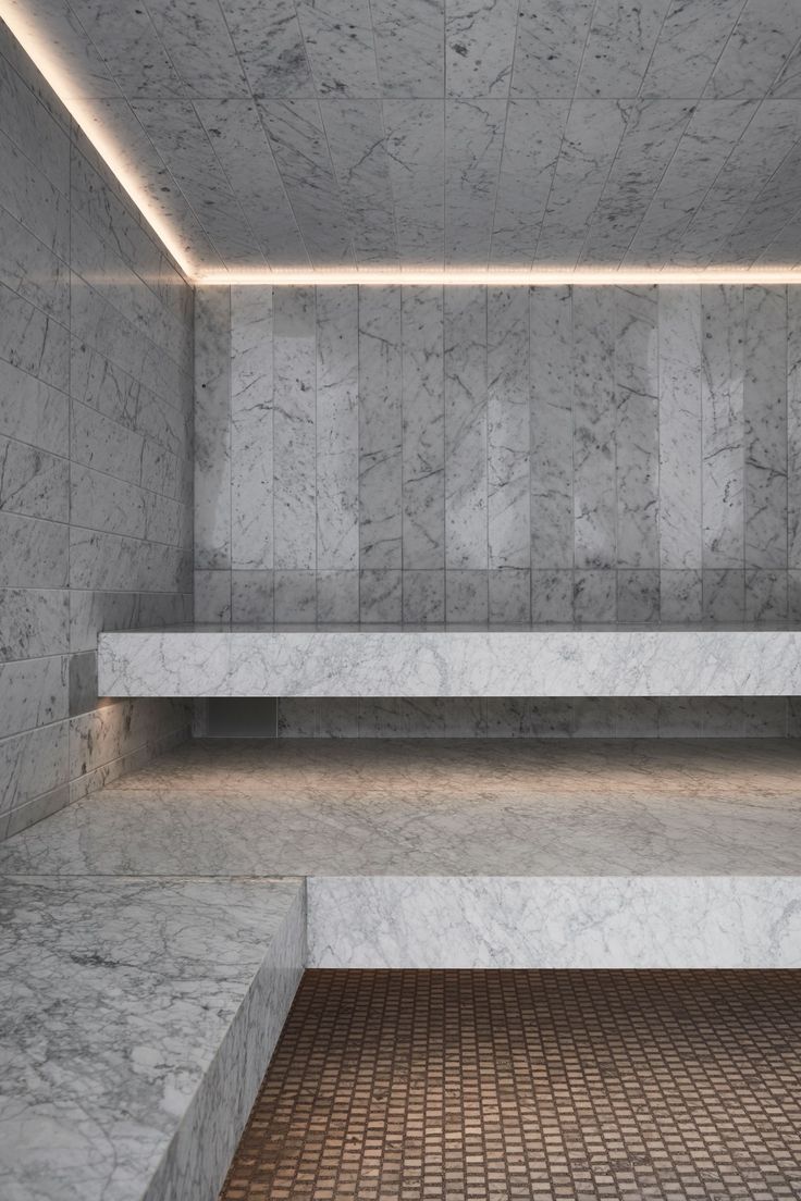 an empty room with marble walls and tiled flooring, illuminated by recessed lighting