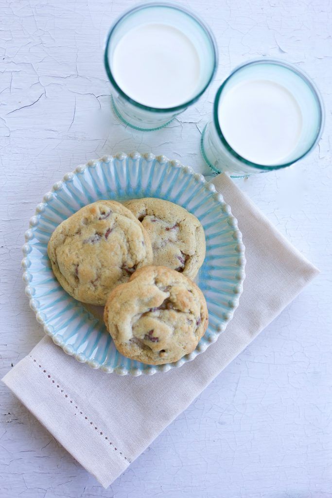 chocolate chip cookies on a blue plate next to two glasses of milk and a napkin