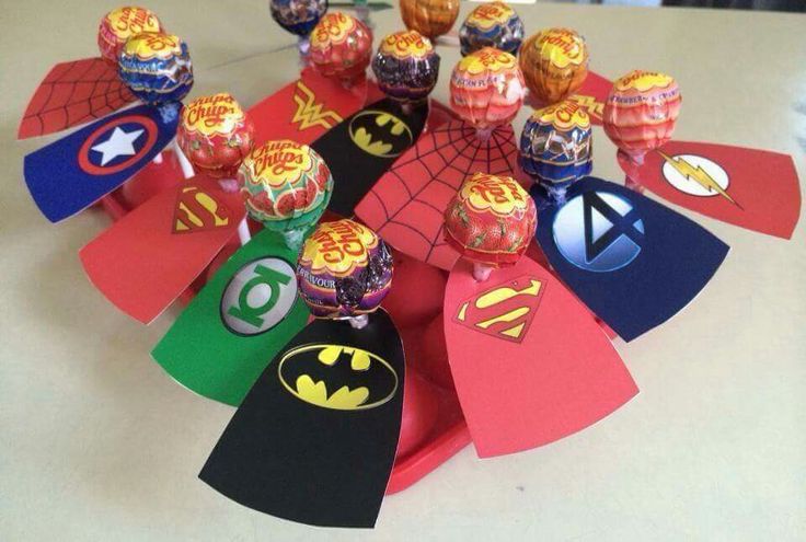 a bunch of candy on top of a table with batman and captain america decorations around it