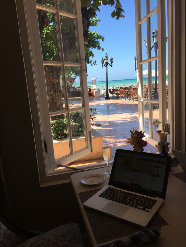 an open laptop computer sitting on top of a wooden table next to a large window