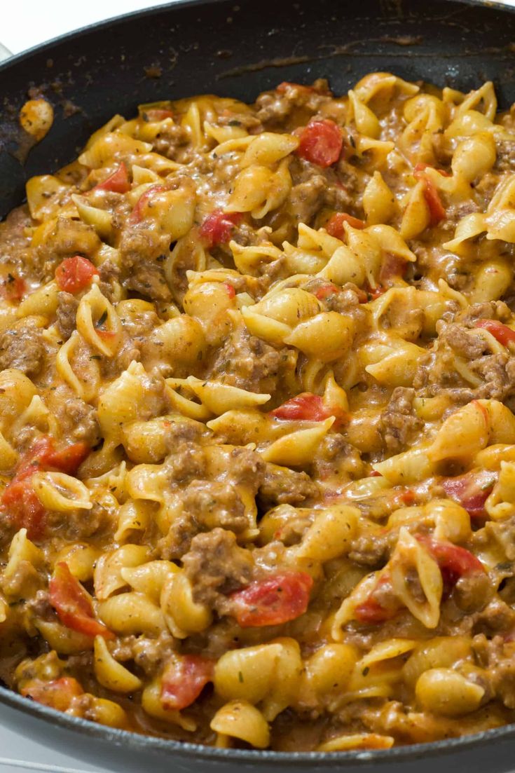 a skillet with pasta and meat in it on top of a stove burner