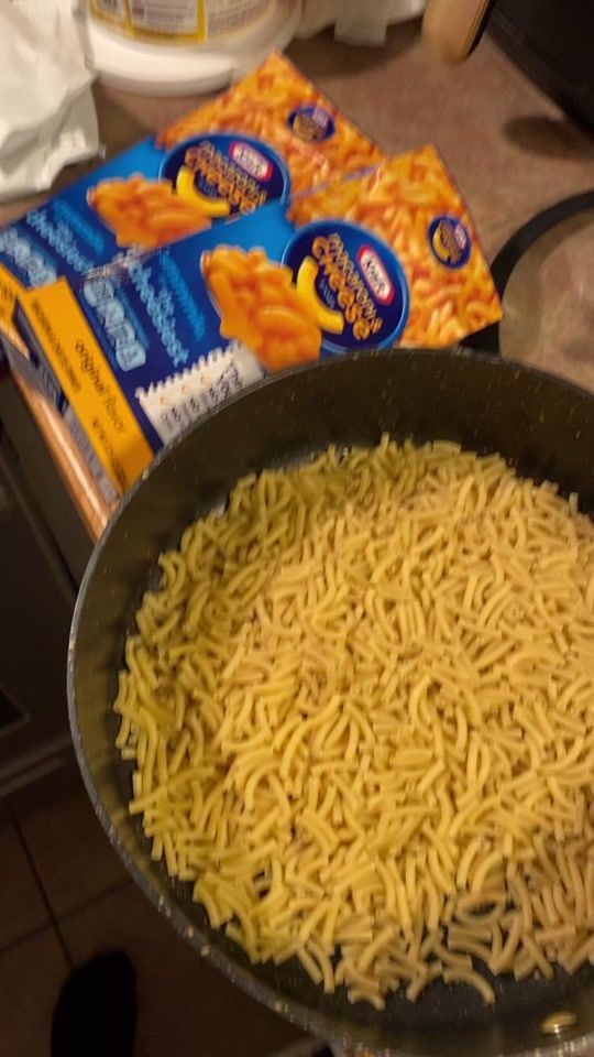 a frying pan filled with noodles next to two packages of cheese and potato chips