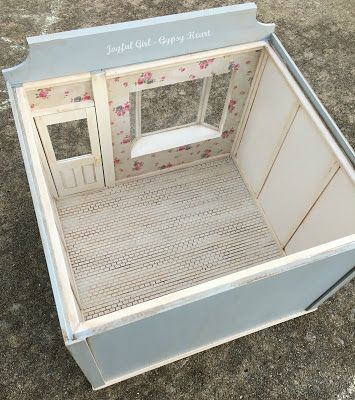 an old fashioned dollhouse with the door open and window closed, sitting on concrete ground