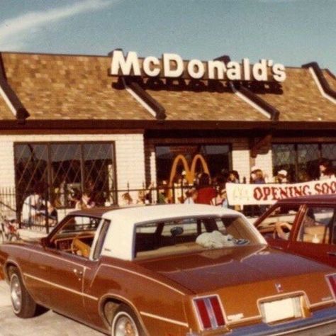 two cars parked in front of a mcdonald's with people standing outside the building