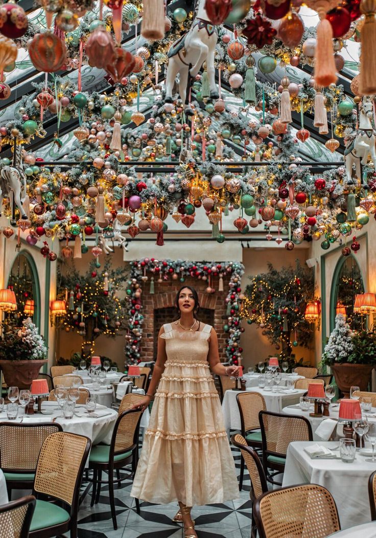 a woman standing in the middle of a room filled with tables and chairs covered in christmas decorations