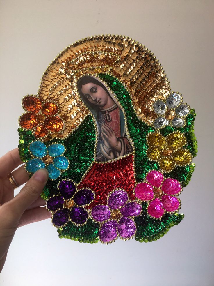 a hand holding up a colorful brooch with an image of the virgin mary on it