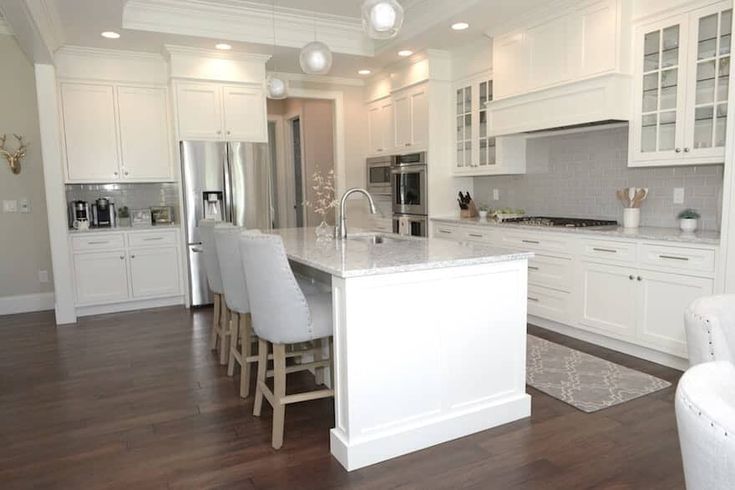 a large kitchen with white cabinets and counter tops, along with bar stools that match the hardwood flooring