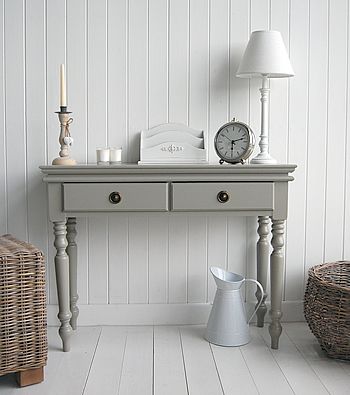 a table with a clock, lamp and vase on it in a room that has white walls