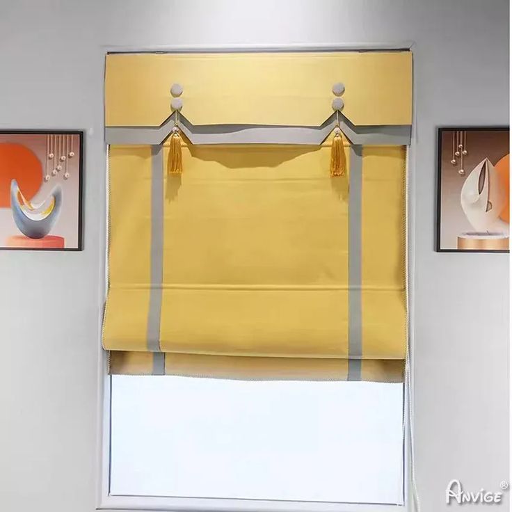 a yellow roman blind hanging on the side of a window in a room with three pictures above it