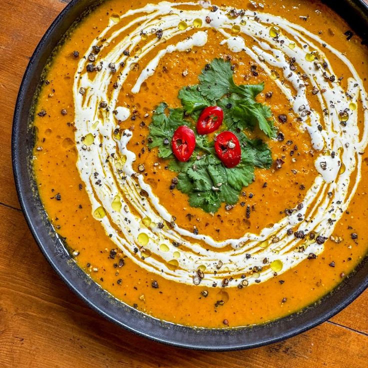 a black bowl filled with soup and topped with sour cream, garnished with fresh herbs