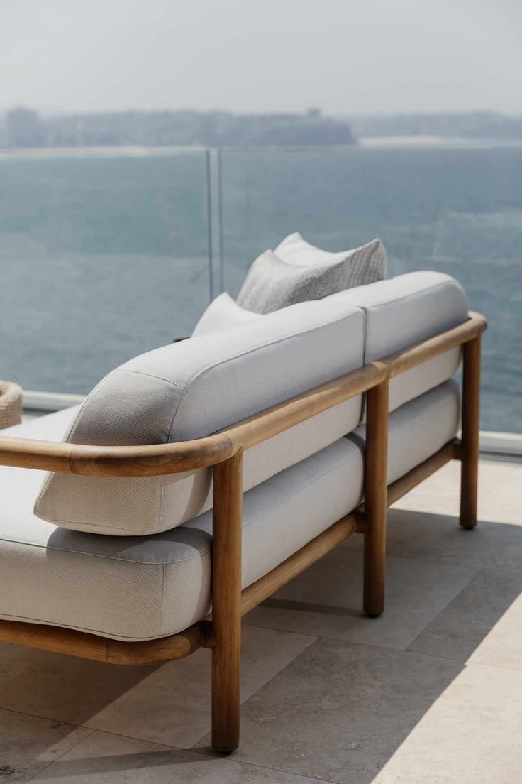 a white couch sitting on top of a wooden floor next to the ocean and sky