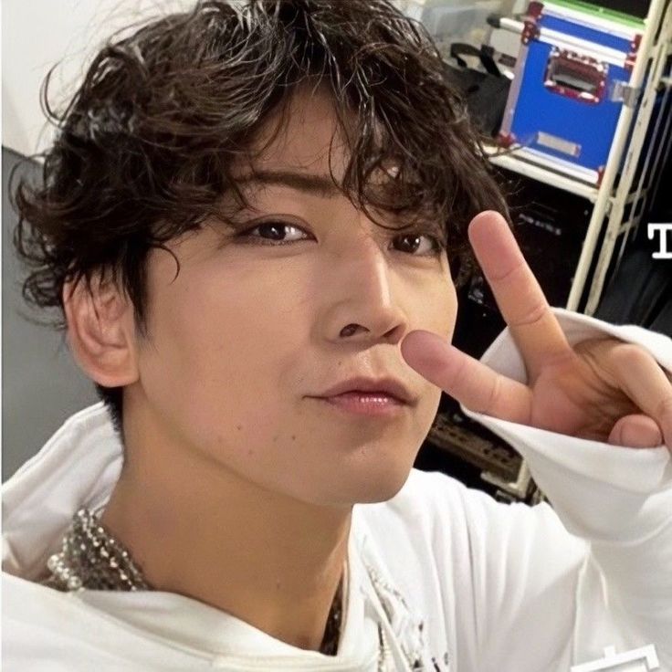 a young man making the peace sign with his hand and wearing a white shirt in front of him