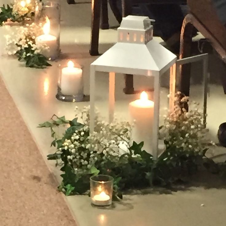 candles are lit on the ground with flowers and greenery around them, along with small white lanterns