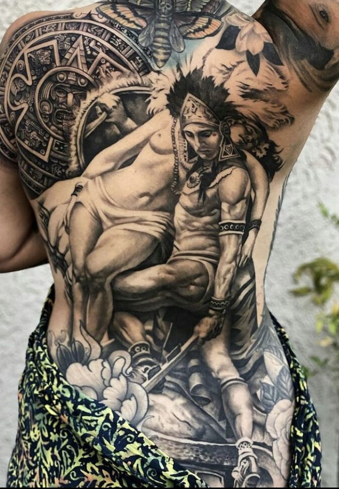 a man with tattoos on his back is standing in front of a white wall and has an image of two men