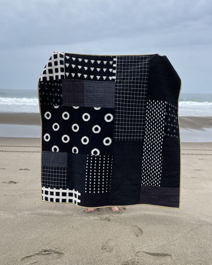 a black and white patchwork quilt on the beach with footprints in the sand next to it