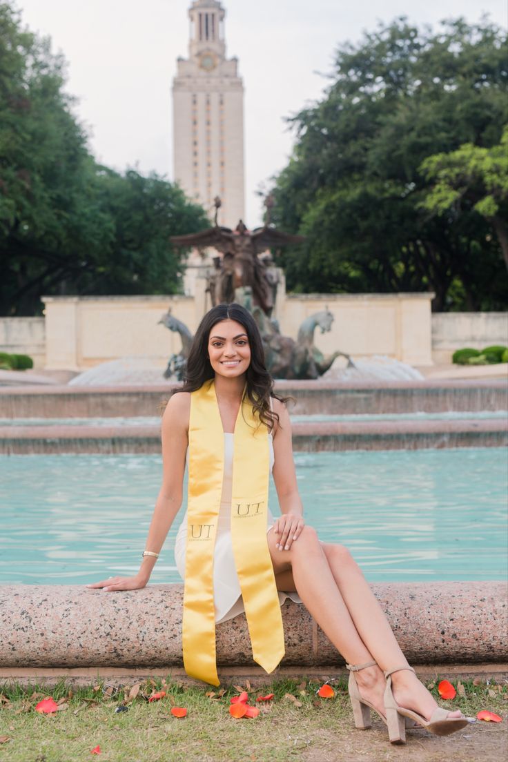 a woman sitting in front of a fountain wearing a yellow sash