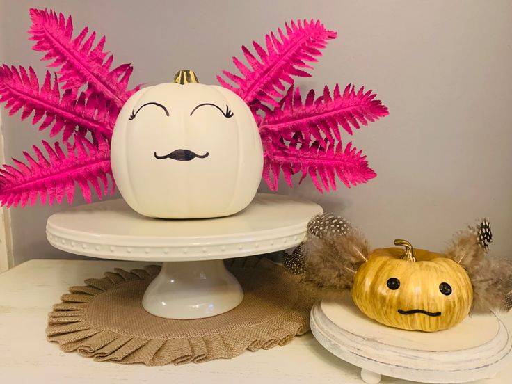 a white pumpkin sitting on top of a cake plate next to a pink fake fern