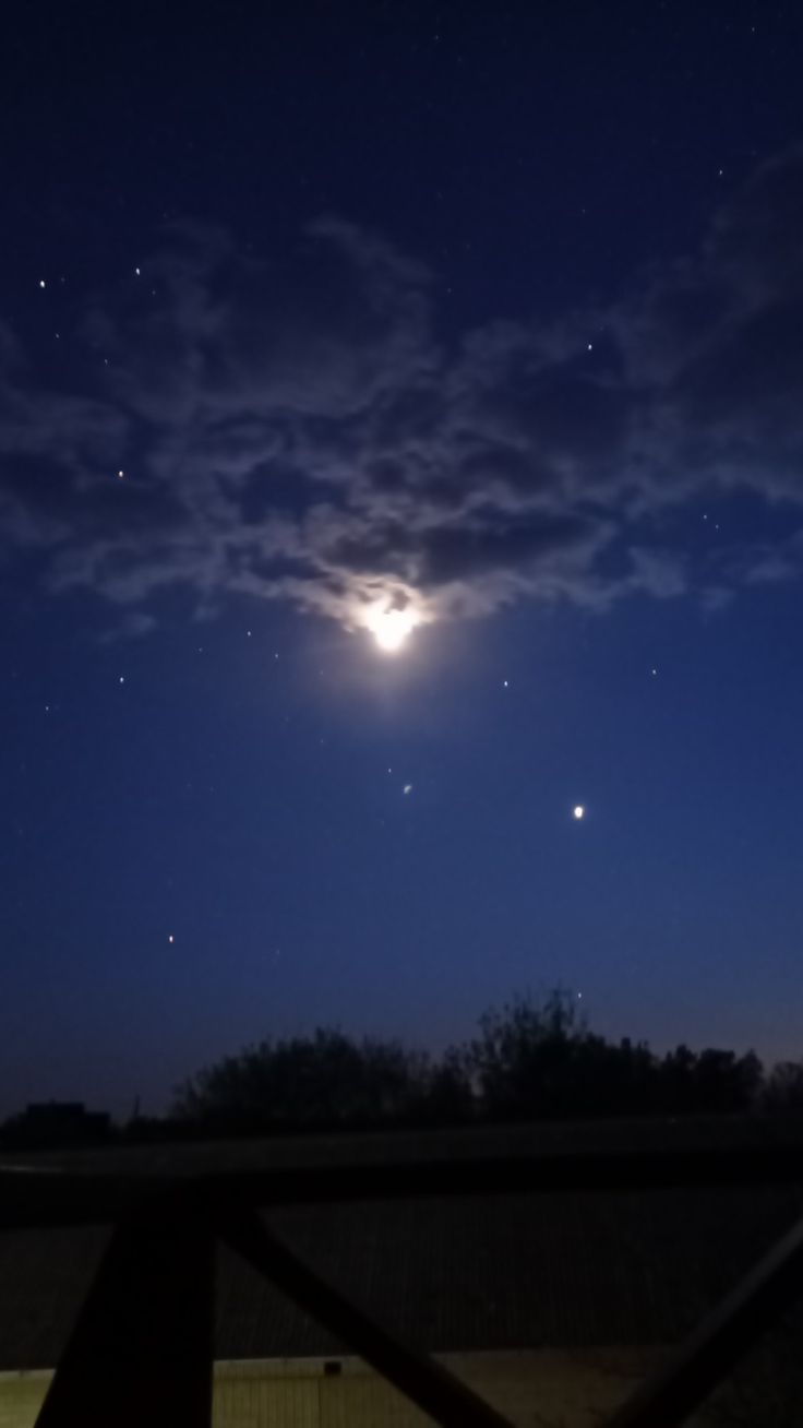 the moon and venus are seen in the night sky over a fenced area with trees