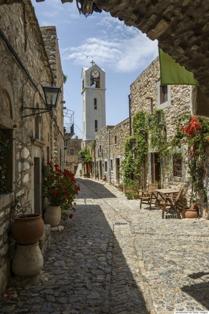 an alley way with tables and chairs on the side, and a clock tower in the background