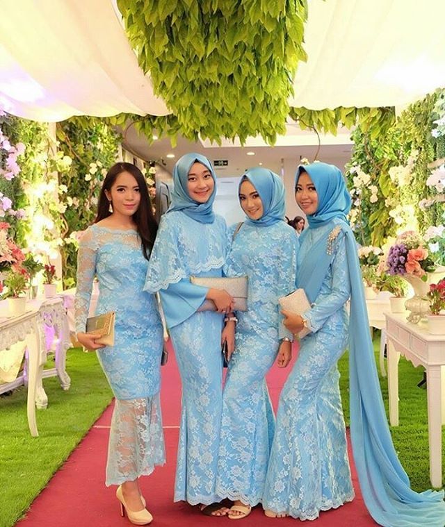 four women in blue dresses standing on a red carpet under a canopy with flowers and greenery behind them