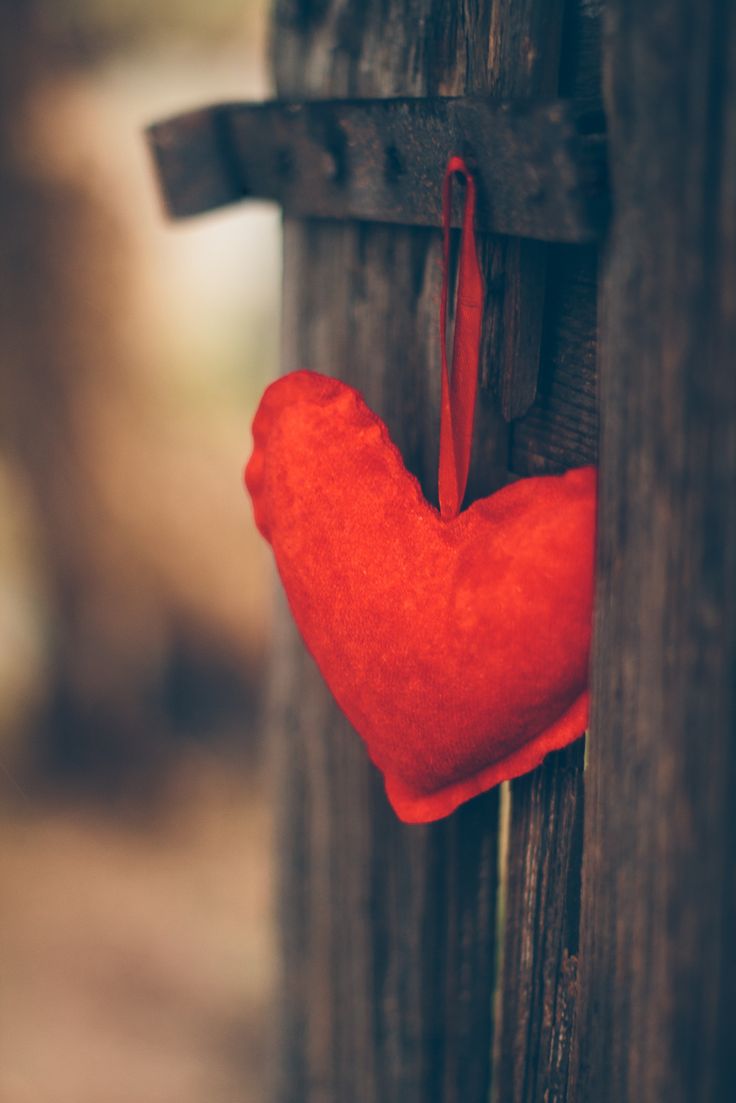 a red heart hanging on the side of a wooden fence