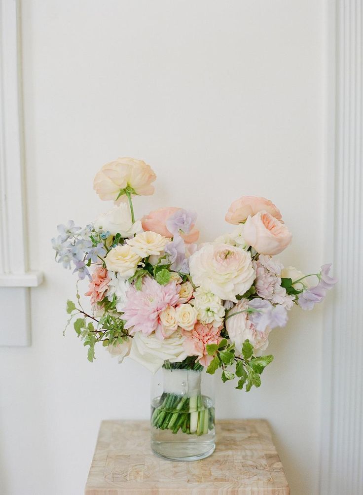 a vase filled with lots of flowers on top of a wooden table next to a white wall