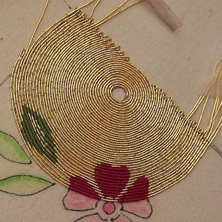 a close up of a piece of gold wire on a white cloth with flowers and leaves