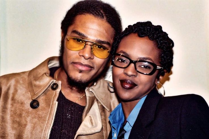 a man and woman are posing for a photo in front of a white wall wearing glasses