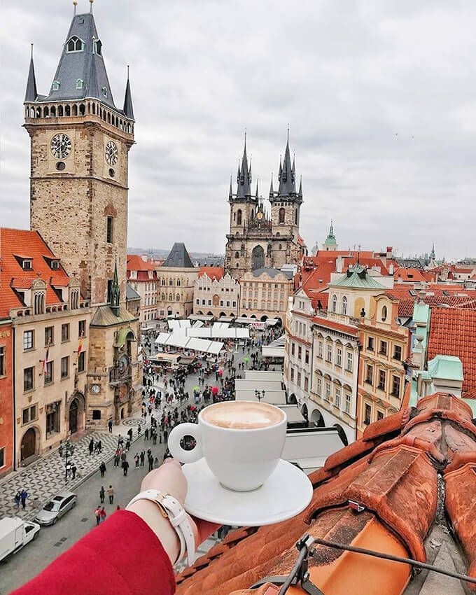 a cup of coffee sitting on top of a roof next to a tall clock tower