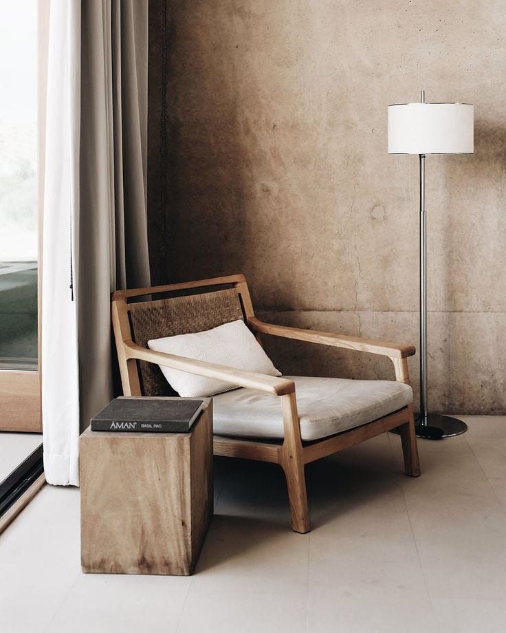 a living room with a chair and lamp next to a window on the floor, in front of a concrete wall