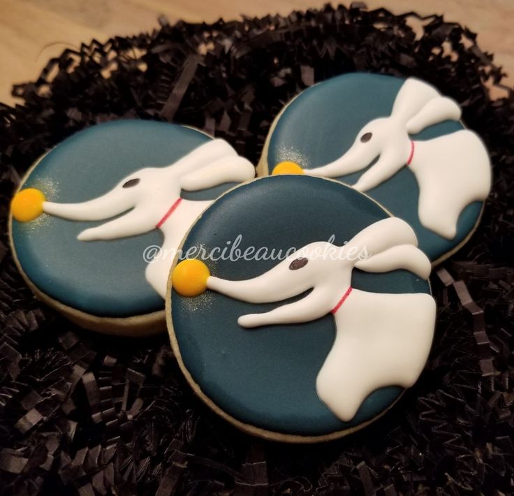 three decorated cookies in the shape of ghost's on top of black shredded paper